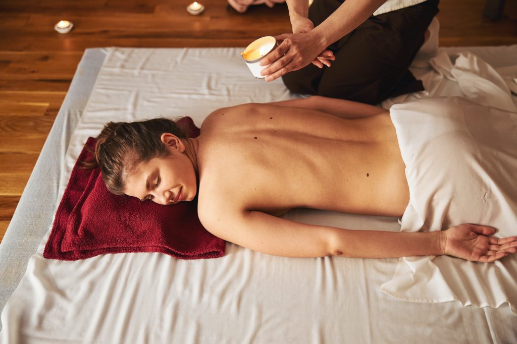 Massagist bringing massage candle to naked female back